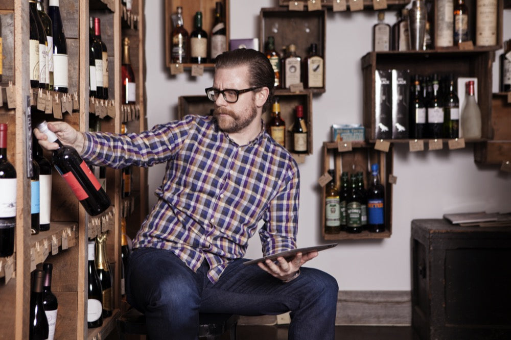 Mann im Weinladen schaut sich ein Etikett an und fragt sich: "Was steht eigentlich auf einem Weinetikett und warum?"